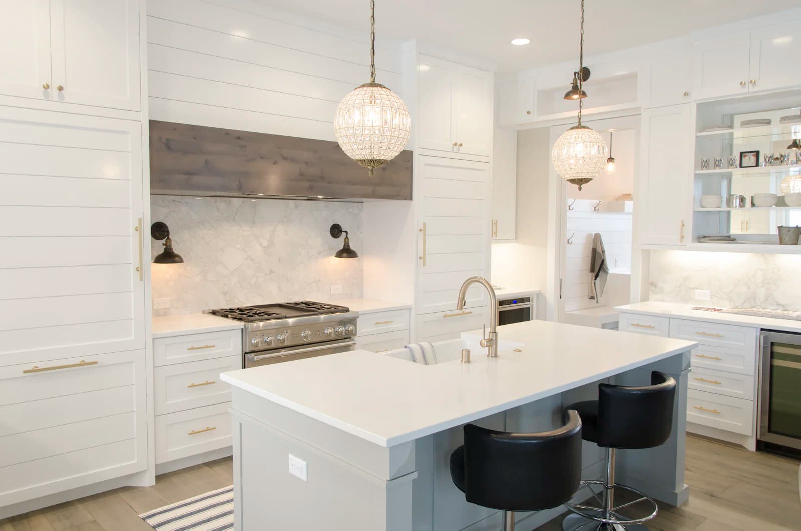 A luxury white kitchen with a marble island, brushed-brass hardware, and crystal pendant lighting.